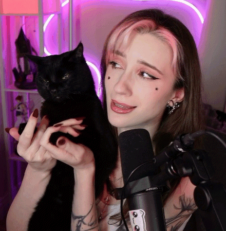A Woman Holding A Black Cat In Front Of A Microphone That Says Shure GIF
