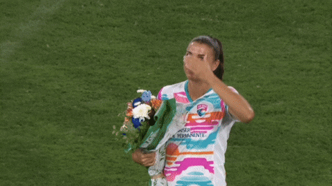 A Woman Holding A Bouquet Of Flowers And Wearing A Shirt That Says ' Uber Permanente ' On It GIF