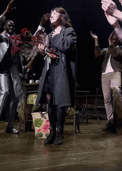 A Woman Holding A Bouquet Of Flowers Stands On A Stage GIF