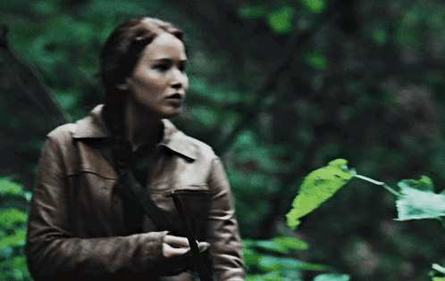 A Woman Holding A Bow And Arrow Standing Next To A Tree GIF