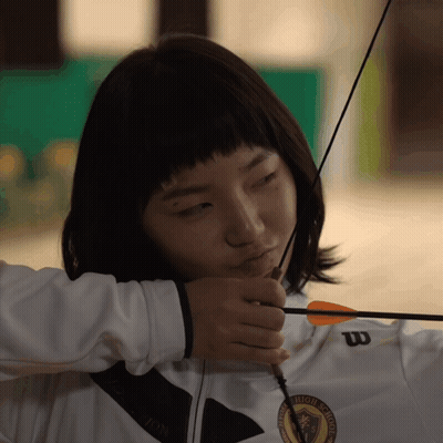 A Woman Holding A Bow And Arrow Wearing A White Wilson Jacket GIF