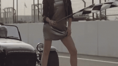 A Woman Holding A Checkered Flag In Front Of A Car That Says Intercity Academy GIF