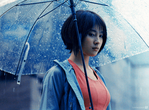 A Woman Holding A Clear Umbrella In The Rain With A Livingship Logo Behind Her GIF