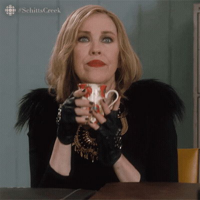 A Woman Holding A Cup Of Coffee With The Hashtag Schitts Creek GIF