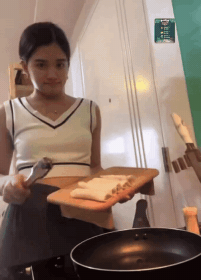 A Woman Holding A Cutting Board Next To A Frying Pan With A Sticker On The Wall That Says ' A ' GIF