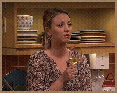 A Woman Holding A Glass Of Wine In Front Of A Shelf With Plates GIF