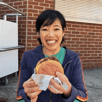 A Woman Holding A Mcdonald 'S Hamburger In Front Of A Brick Building GIF
