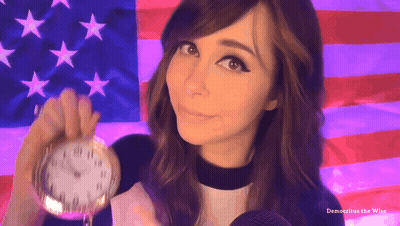 A Woman Holding A Pocket Watch In Front Of An American Flag With The Words Democritus The Wise Below Her GIF
