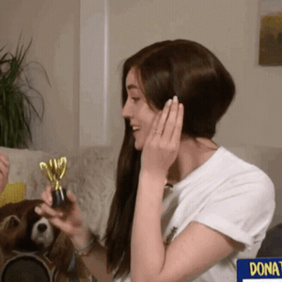 A Woman Holding A Trophy In Front Of A Sign That Says " Donate " GIF