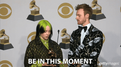 A Woman Holding A Trophy Next To A Man With The Words Be In This Moment On The Bottom GIF