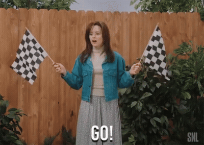 A Woman Holding Two Checkered Flags And Says Go GIF