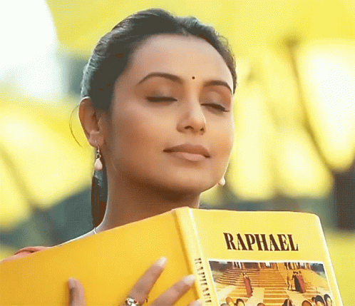 A Woman Holds A Book Titled Raphael In Her Hands GIF