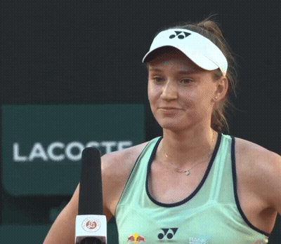 A Woman Holds A Microphone In Front Of A Lacoste Sign GIF