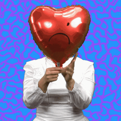 A Woman Holds A Red Heart Shaped Balloon With A Sad Face On It GIF