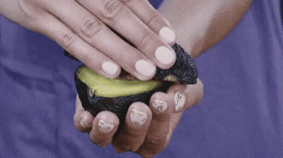 A Woman Holds A Sliced Avocado In Her Hand GIF