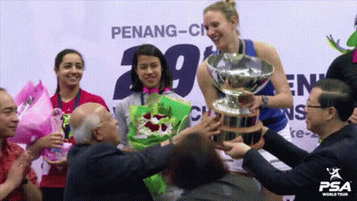 A Woman Holds A Trophy In Front Of A Penang-City Sign GIF