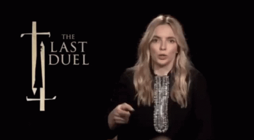 A Woman Holds A Trophy In Front Of A Sign That Says The Last Duel GIF