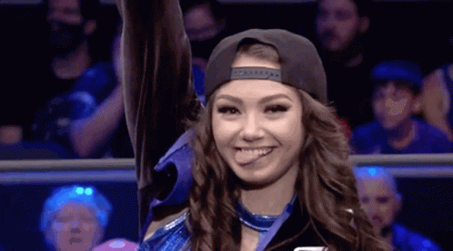 A Woman In A Baseball Cap Is Smiling And Holding Up Her Hand In A Ring . GIF