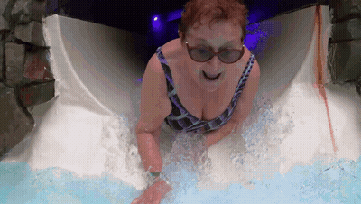 A Woman In A Bathing Suit And Sunglasses Slides Down A Water Slide GIF