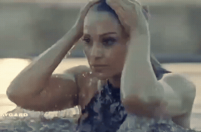 A Woman In A Bathing Suit Is Standing In A Pool Holding Her Head . GIF