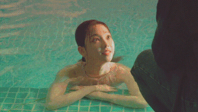 A Woman In A Bathing Suit Is Swimming In A Pool With A Person Standing Behind Her GIF