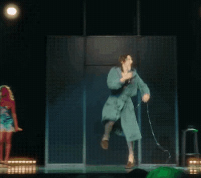 A Woman In A Bathrobe Is Dancing On A Stage GIF