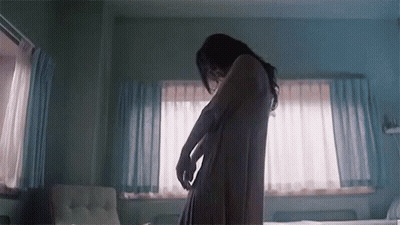 A Woman In A Bathrobe Is Standing In A Bedroom . GIF