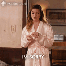 A Woman In A Bathrobe Is Standing In Front Of A Couch And Says I 'M Sorry . GIF