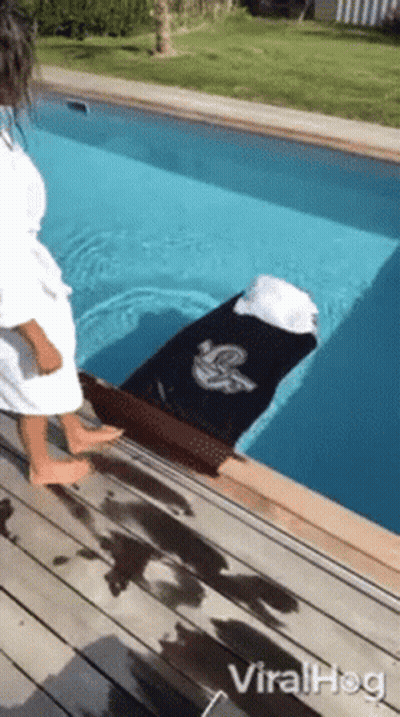 A Woman In A Bathrobe Is Standing Next To A Swimming Pool With A Coffin In It . GIF