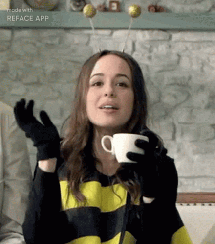 A Woman In A Bee Costume Is Holding A Cup Of Coffee In Her Hands . GIF