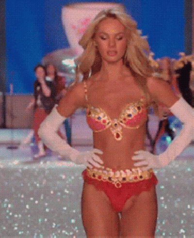A Woman In A Bikini And White Gloves Is Walking On A Runway GIF