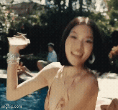A Woman In A Bikini Is Holding A Drink In Her Hand In Front Of A Swimming Pool . GIF