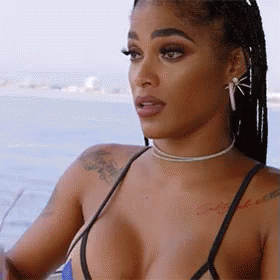 A Woman In A Bikini Is Sitting On A Boat Looking At The Water . GIF