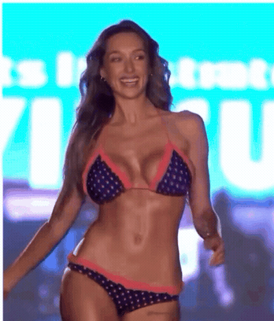 A Woman In A Bikini Is Smiling In Front Of A Sign That Says ' It 'S In ' GIF