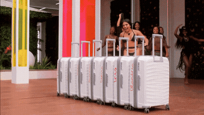 A Woman In A Bikini Is Standing In Front Of A Row Of Suitcases That Say Travis And Andrew On Them GIF