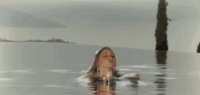 A Woman In A Bikini Is Standing In The Water . GIF