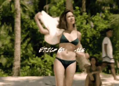 A Woman In A Bikini Is Standing On A Beach Holding A Towel And The Words " Free By Me " Are Visible GIF