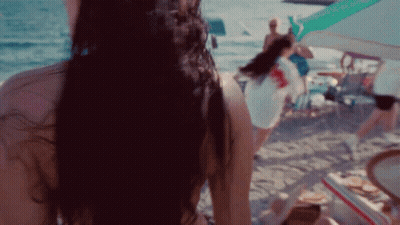 A Woman In A Bikini Is Standing On A Beach Looking At The Ocean GIF