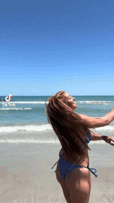 A Woman In A Bikini Is Standing On The Beach With Her Arms Outstretched . GIF