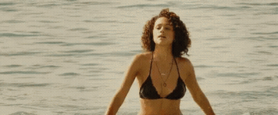 A Woman In A Bikini Is Walking Along The Beach . GIF