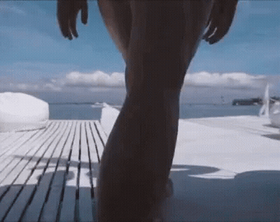 A Woman In A Bikini Is Walking On A Wooden Deck Towards The Ocean GIF