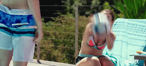 A Woman In A Bikini Sits On A Chair Next To A Man In Swim Shorts GIF
