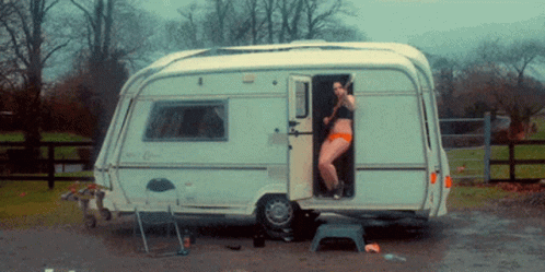 A Woman In A Bikini Stands In The Doorway Of A Camper GIF
