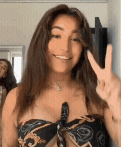 A Woman In A Bikini Top Is Giving A Peace Sign And Smiling In Front Of A Mirror . GIF