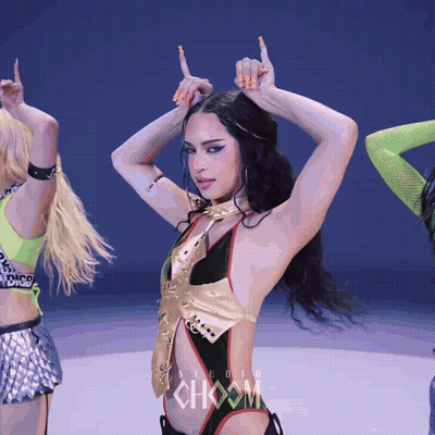 A Woman In A Black And Gold Bodysuit Is Dancing In Front Of A Sign That Says Choom GIF