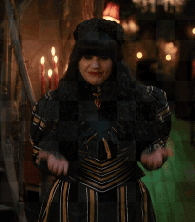 A Woman In A Black And Gold Dress Is Standing In A Dark Room GIF