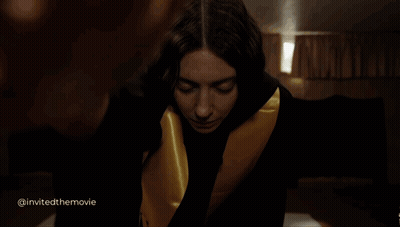 A Woman In A Black And Gold Robe Is Looking At The Camera With The Words Invited The Movie Below Her GIF