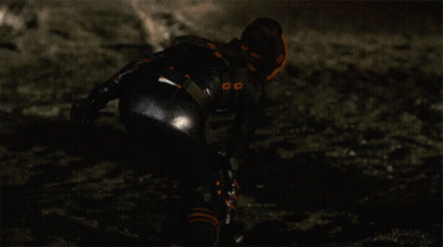 A Woman In A Black And Orange Outfit Is Kneeling Down GIF