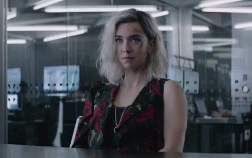 A Woman In A Black And Red Dress Is Sitting At A Table GIF
