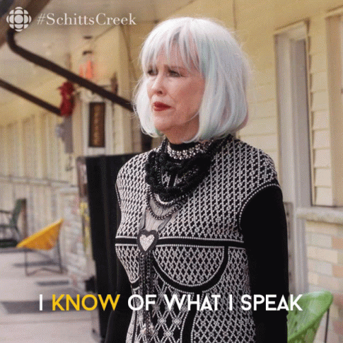 A Woman In A Black And White Dress Says " I Know Of What I Speak " In Front Of A Building GIF